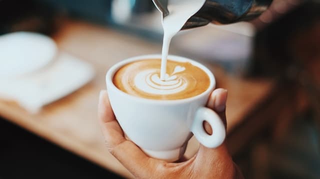 Milk being poured into latte art in a white cup